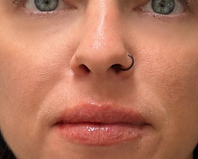 Close-up of a persons face showing green eyes, septum nose piercing, and natural makeup