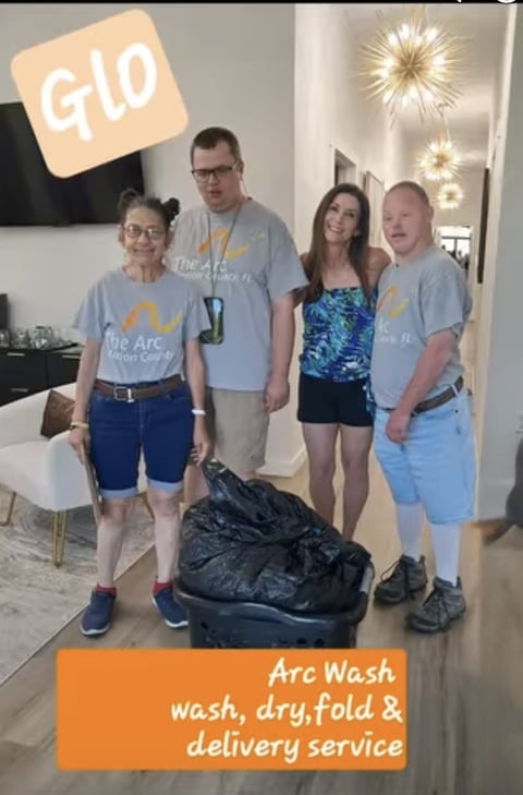 Four people wearing Arc-branded blue t-shirts stand in an office holding a black laundry bag, with G10 logo and Arc Wash service text visible