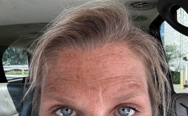 Close-up selfie of a person with gray-blonde hair and blue eyes, taken inside a car